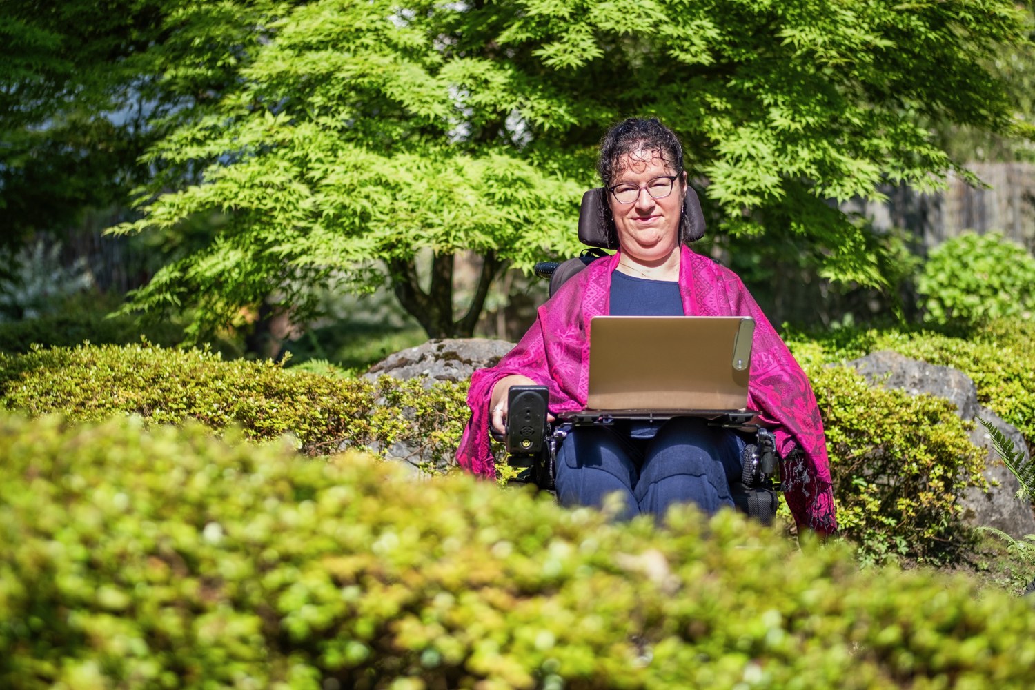 Jenny Thuilier, en fauteuil roulant, avec son ordinateur dans un jardin